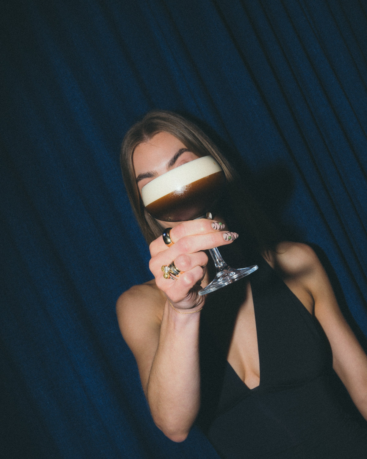 A GRADA espresso martini raised in a coupe against a blue curtain