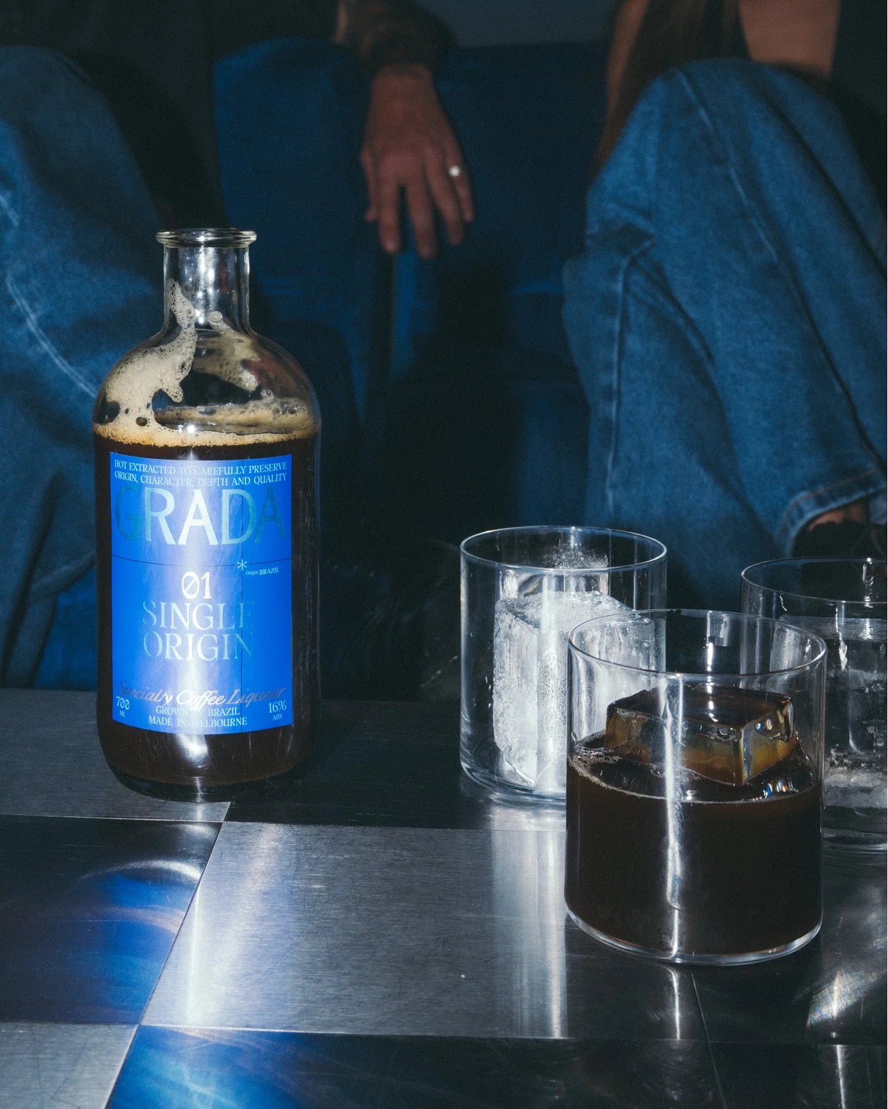 A bottle of GRADA on a reflective table with iced drinks